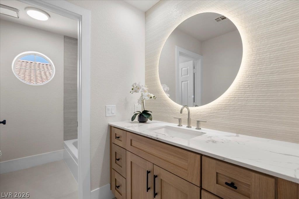 8024 Shorecrest Drive, Las Vegas, NV 89128 A well-appointed bathroom features a light wood vanity, a marble-patterned countertop, and an illuminated mirror.