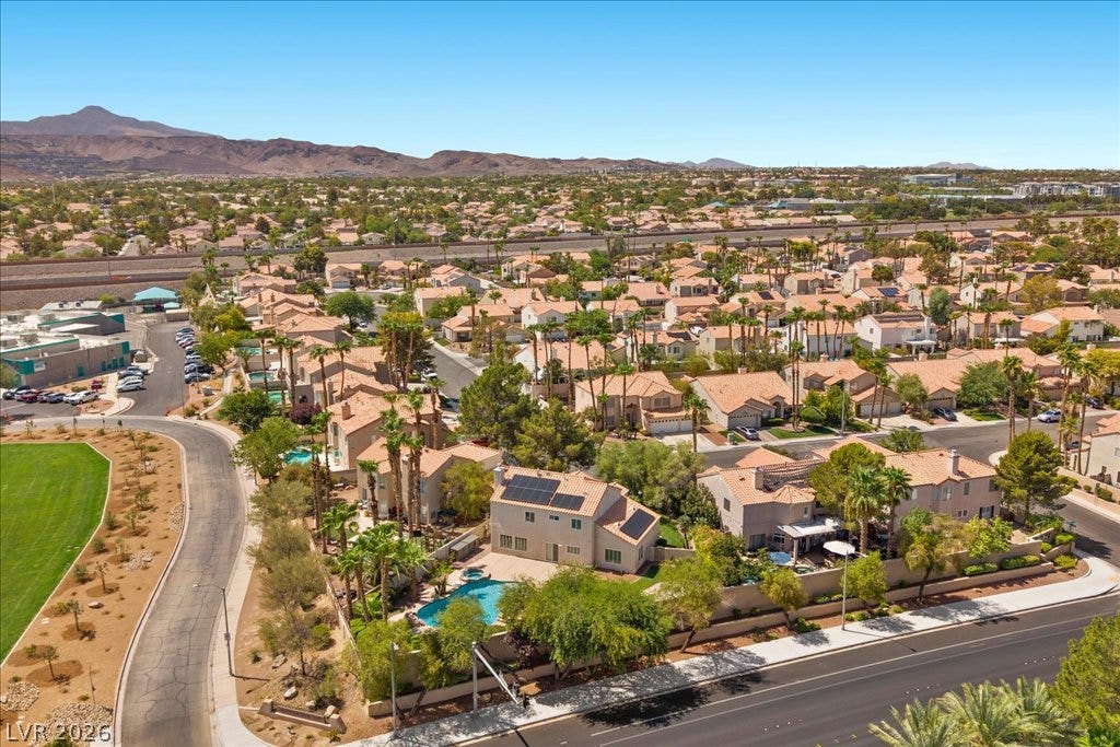 2000 Silverton Drive, Henderson, NV 89074 An aerial perspective reveals a vibrant neighborhood with a home featuring solar panels and a private pool, set against a desert mountain backdrop.