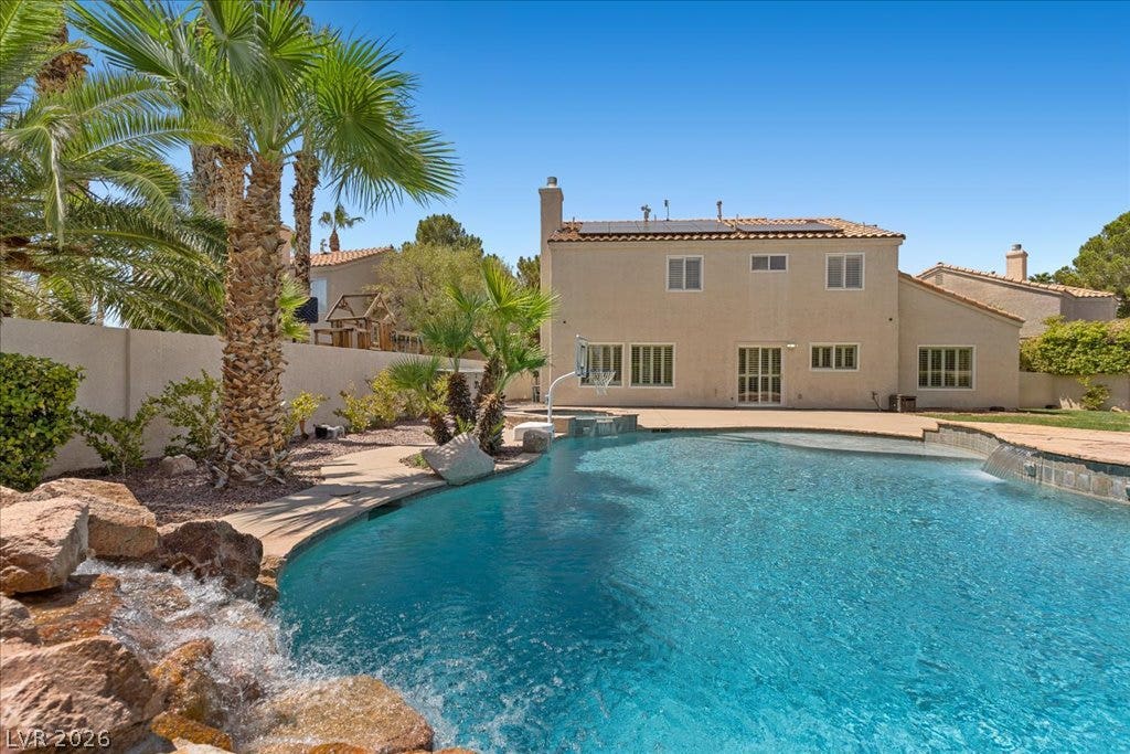 2000 Silverton Drive, Henderson, NV 89074 A tranquil backyard oasis features a glistening pool with a rock waterfall and vibrant palm trees, offering ultimate relaxation.