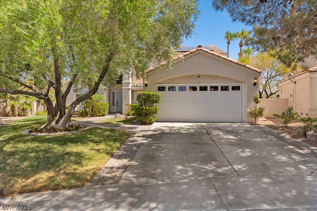 2000 Silverton Drive, Henderson, NV 89074 A welcoming facade features a concrete driveway leading to a two-car garage, framed by verdant trees and manicured landscaping.