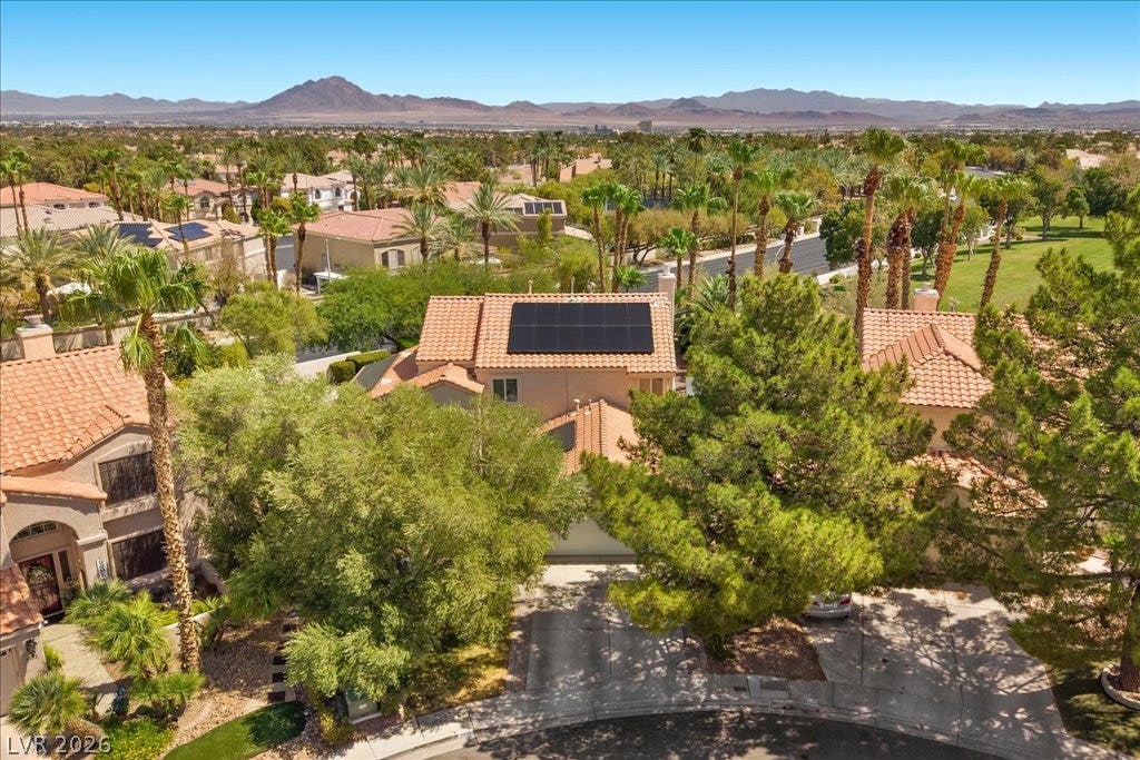 2000 Silverton Drive, Henderson, NV 89074 An aerial perspective reveals a residential neighborhood with tile roofs, solar panels, and abundant greenery against a backdrop of distant mountains.