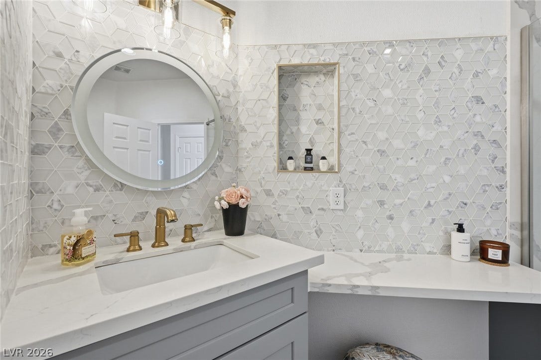 9615 Sedona Hills Court, Las Vegas, NV 89147 Refined bathroom with a contemporary vanity, elegant gold-tone fixtures, and striking geometric tiled walls.
