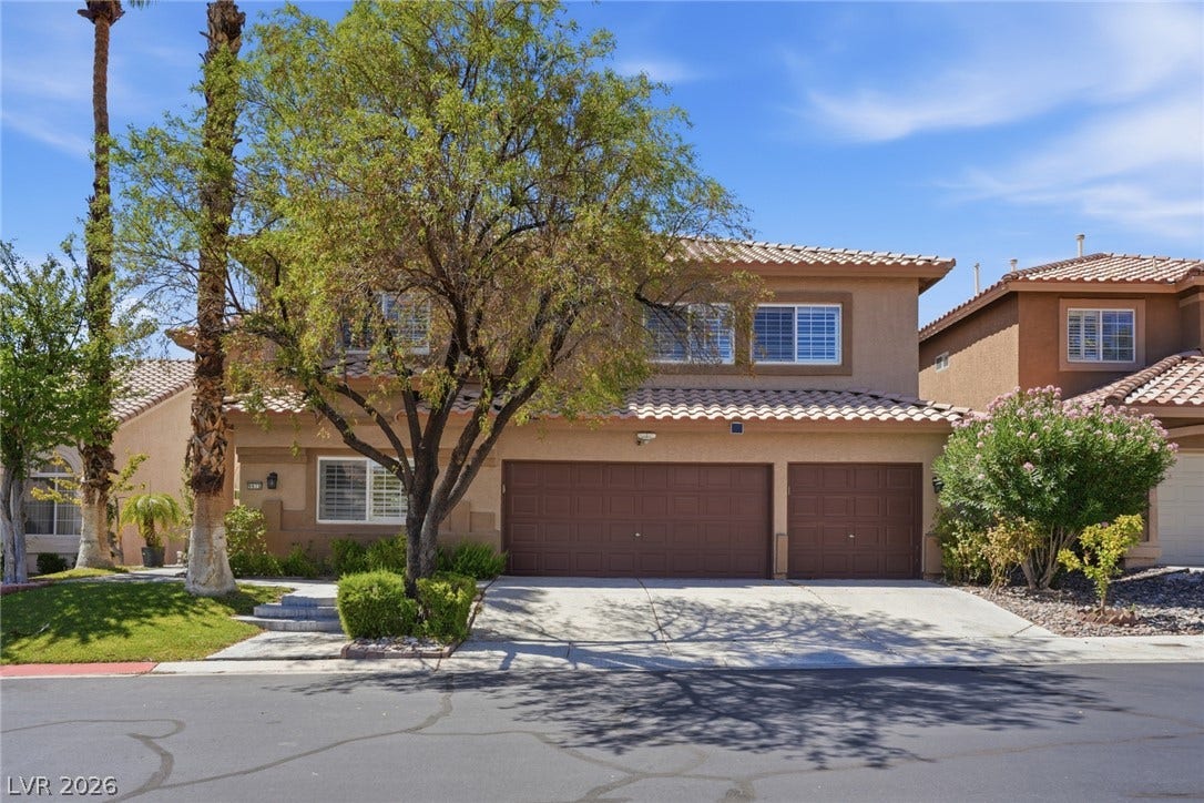9615 Sedona Hills Court, Las Vegas, NV 89147 A terracotta-roofed residence features a broad driveway leading to a two-car garage, framed by lush trees.