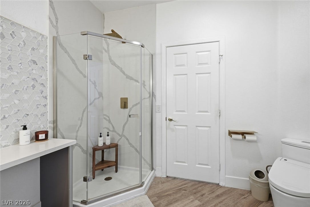 9615 Sedona Hills Court, Las Vegas, NV 89147 A well-appointed primary bathroom showcases a glass-enclosed shower with sophisticated tile work and practical wood flooring.