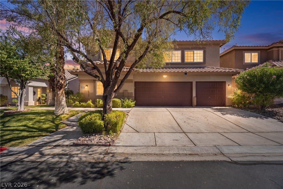 9615 Sedona Hills Court, Las Vegas, NV 89147 A well-maintained facade with mature landscaping frames this two-story home, illuminated by the soft glow of evening.