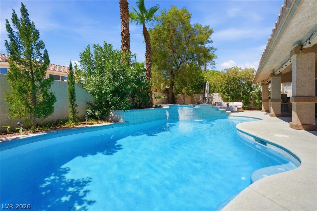 9615 Sedona Hills Court, Las Vegas, NV 89147 An inviting swimming pool and spa cascade with refreshing water, surrounded by lush landscaping and a shaded patio area.