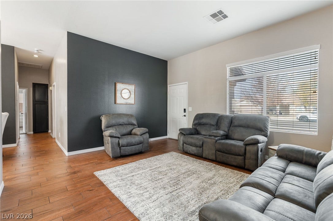 Rich wood-look flooring grounds this open living area with a contrasting accent wall and natural light from wide windows.