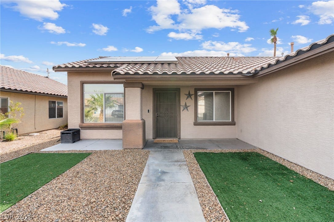 A neatly maintained entryway with a paved walkway welcomes you to this desert home featuring solar panels.