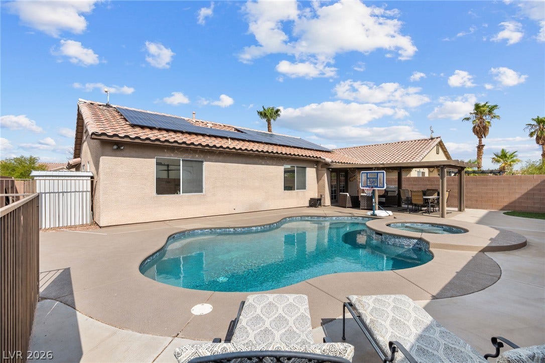 An inviting backyard oasis offers a sparkling pool, spa, and shaded pergola for outdoor enjoyment.
