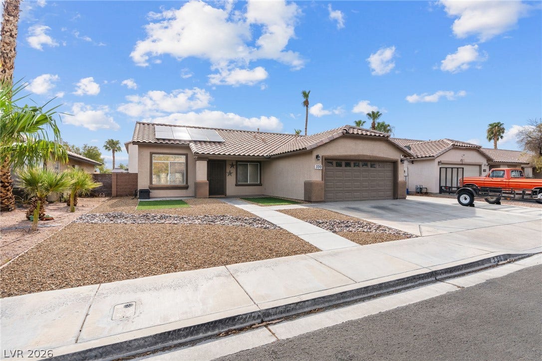 A desert-friendly landscape surrounds this charming stucco residence, featuring an attached garage and practical solar panels and Extra parking