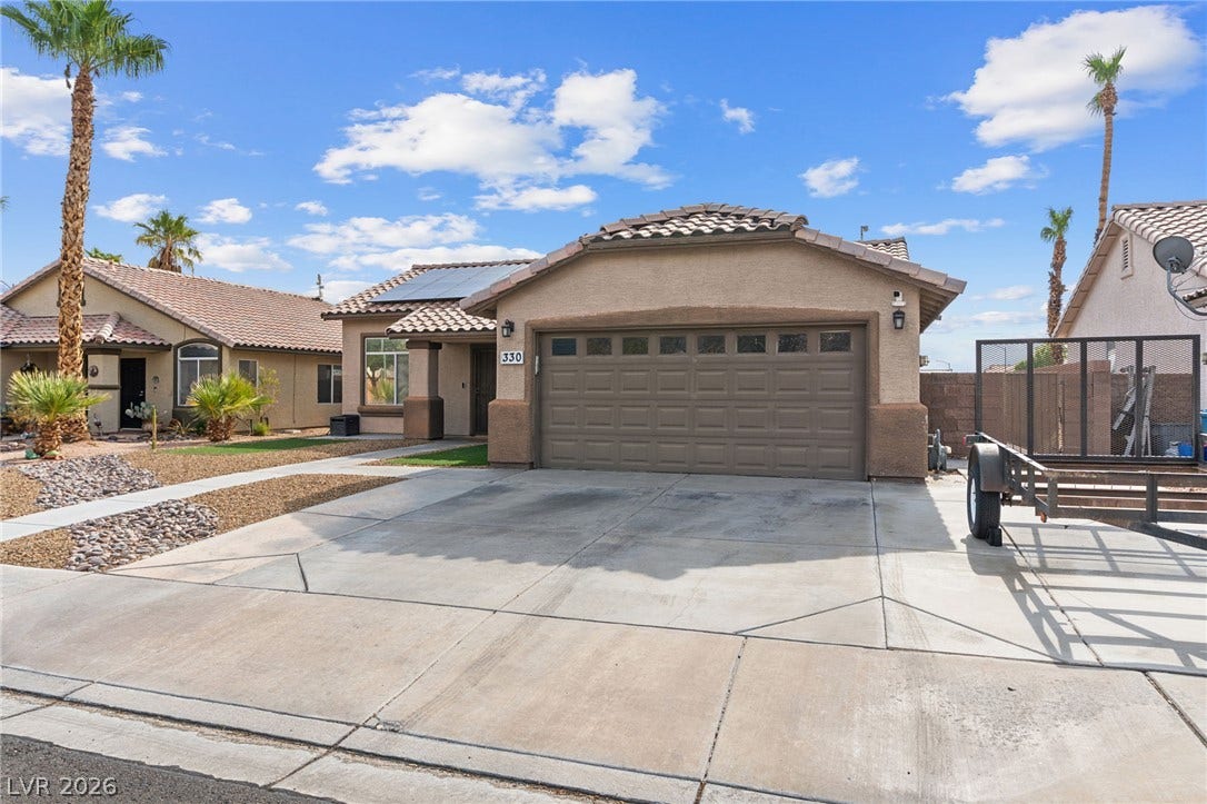 A desert oasis with solar panels, a concrete driveway, and ample parking.