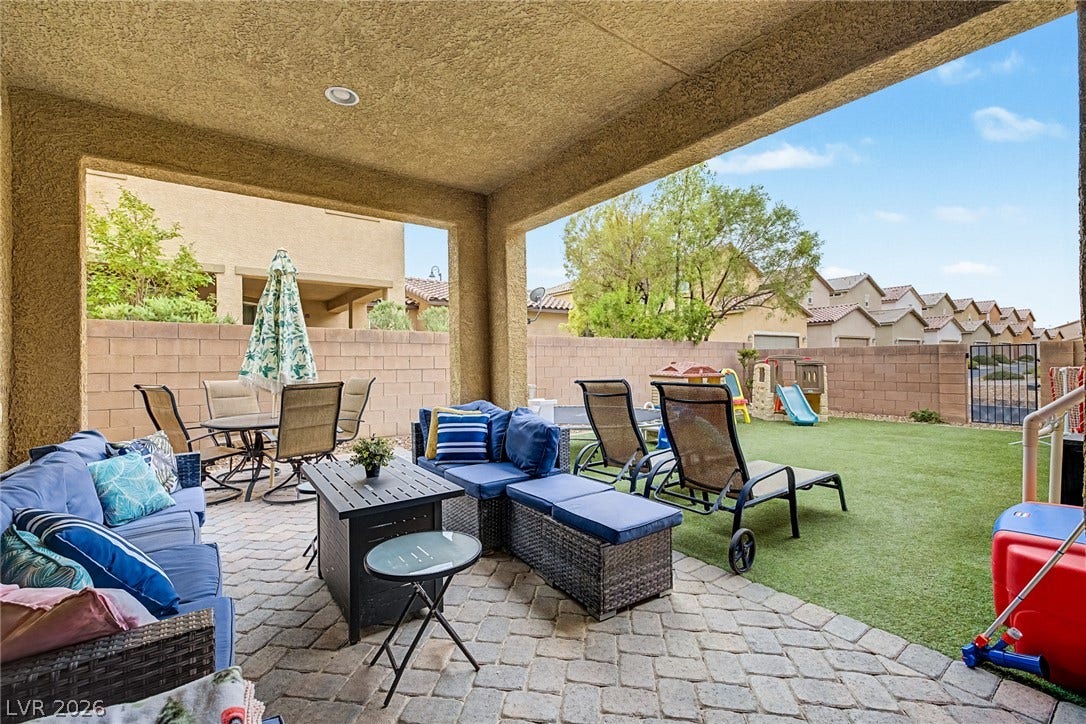 A spacious covered patio with pavers transitions to a grassy yard, offering ample outdoor living and recreation.
