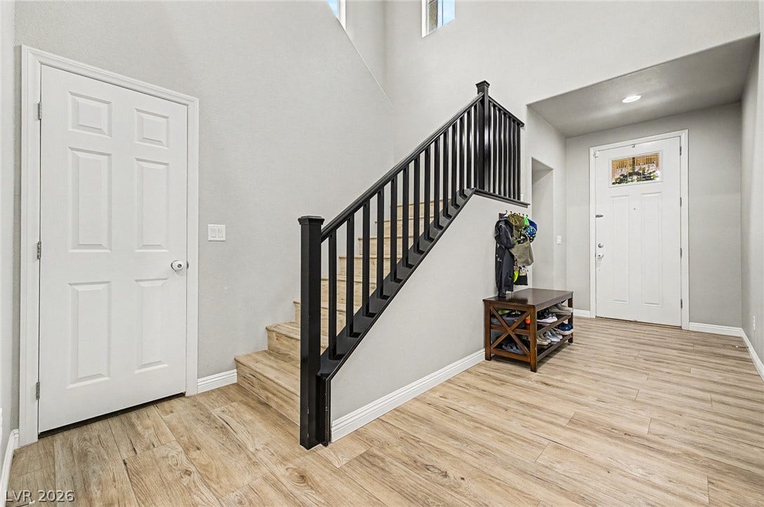 A welcoming entryway features wood-look flooring and a prominent staircase with dark railings, complemented by high ceilings.