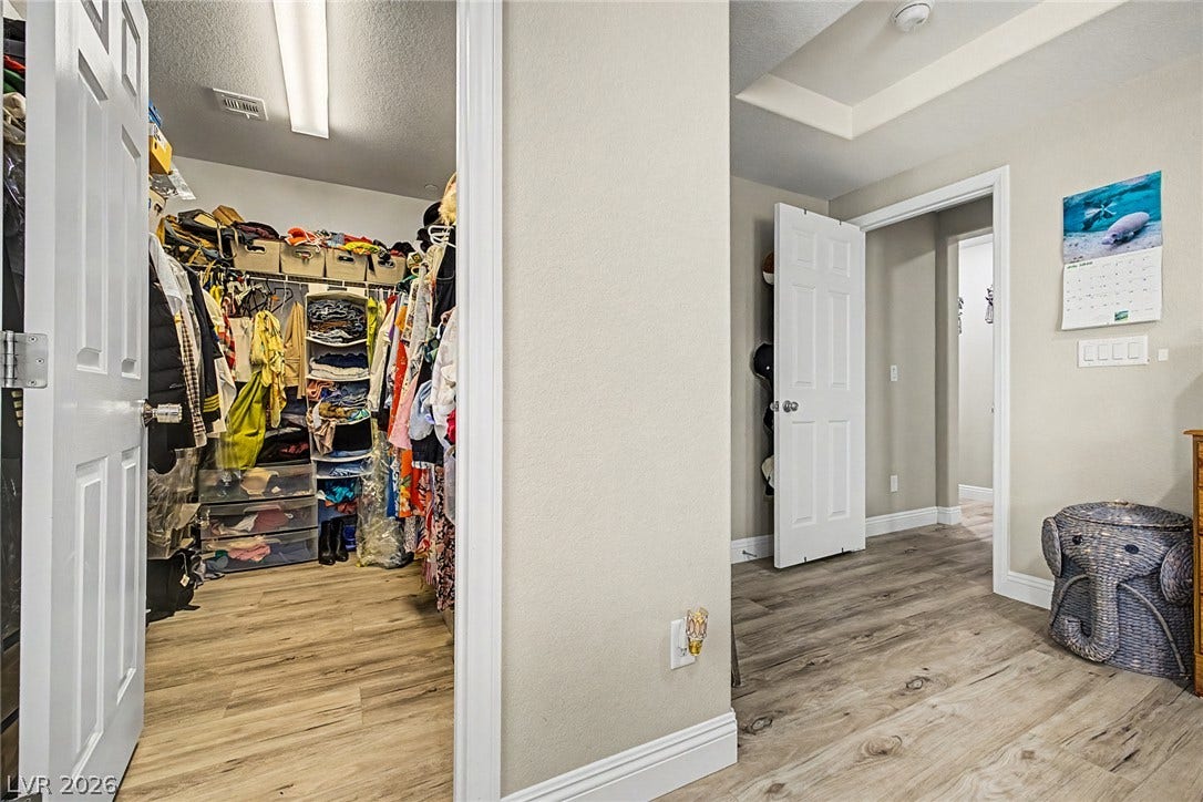 Functional walk-in closet offers ample storage with convenient access from a hallway featuring tray ceilings.