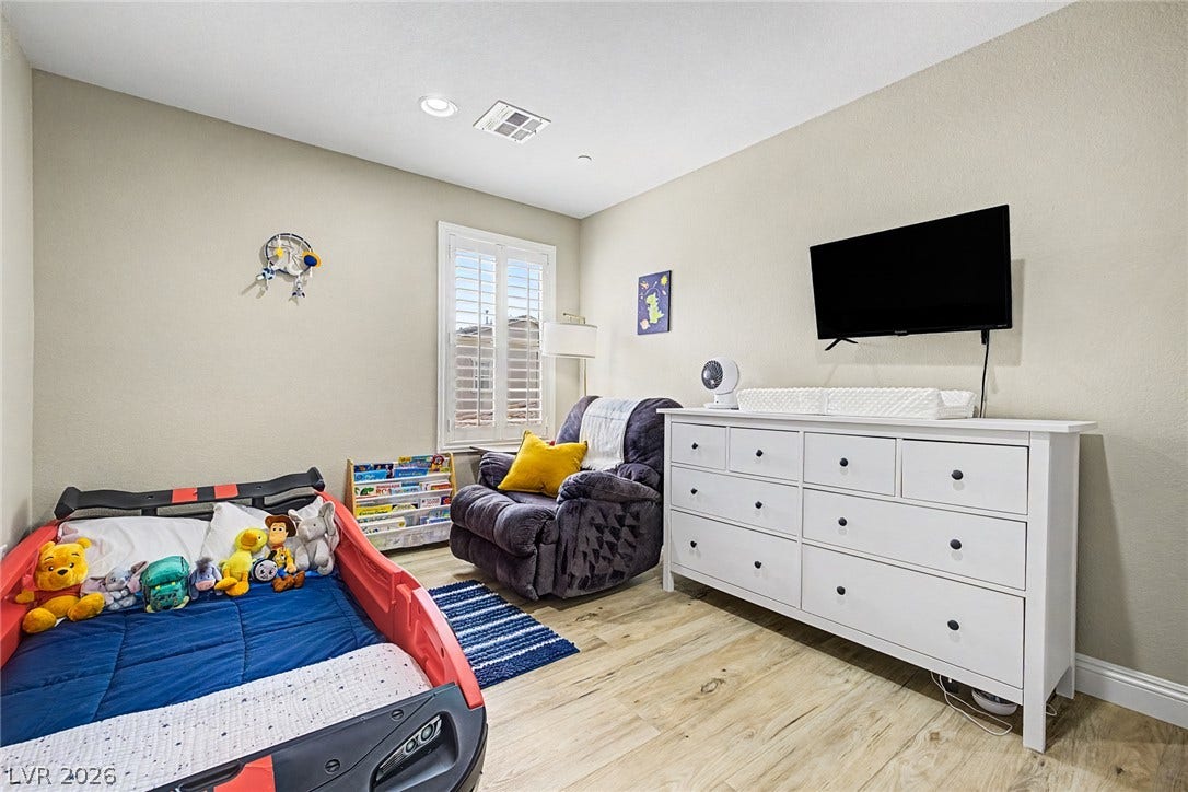 Well-lit nursery featuring durable wood flooring and ample natural light from a window with classic plantation shutters.