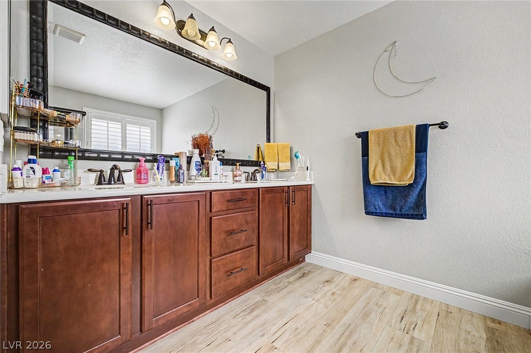 Well-lit primary bathroom featuring a spacious double vanity with ample counter space and elegant wooden cabinetry.