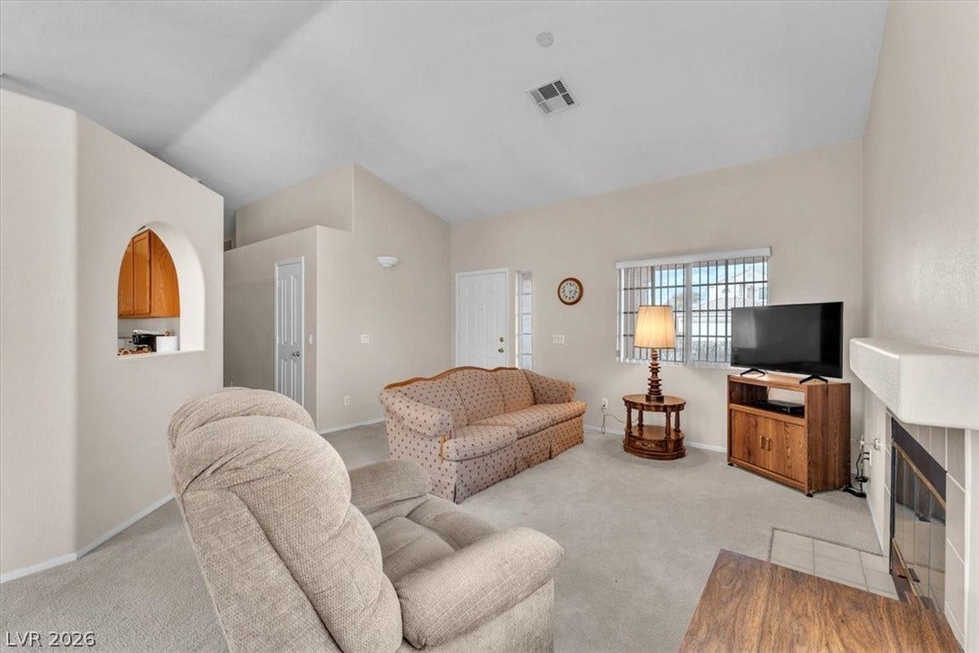 1163 Teal Point Drive, Henderson, NV 89074 Living area with baseboards, visible vents, light colored carpet, lofted ceiling, and a fireplace with flush hearth