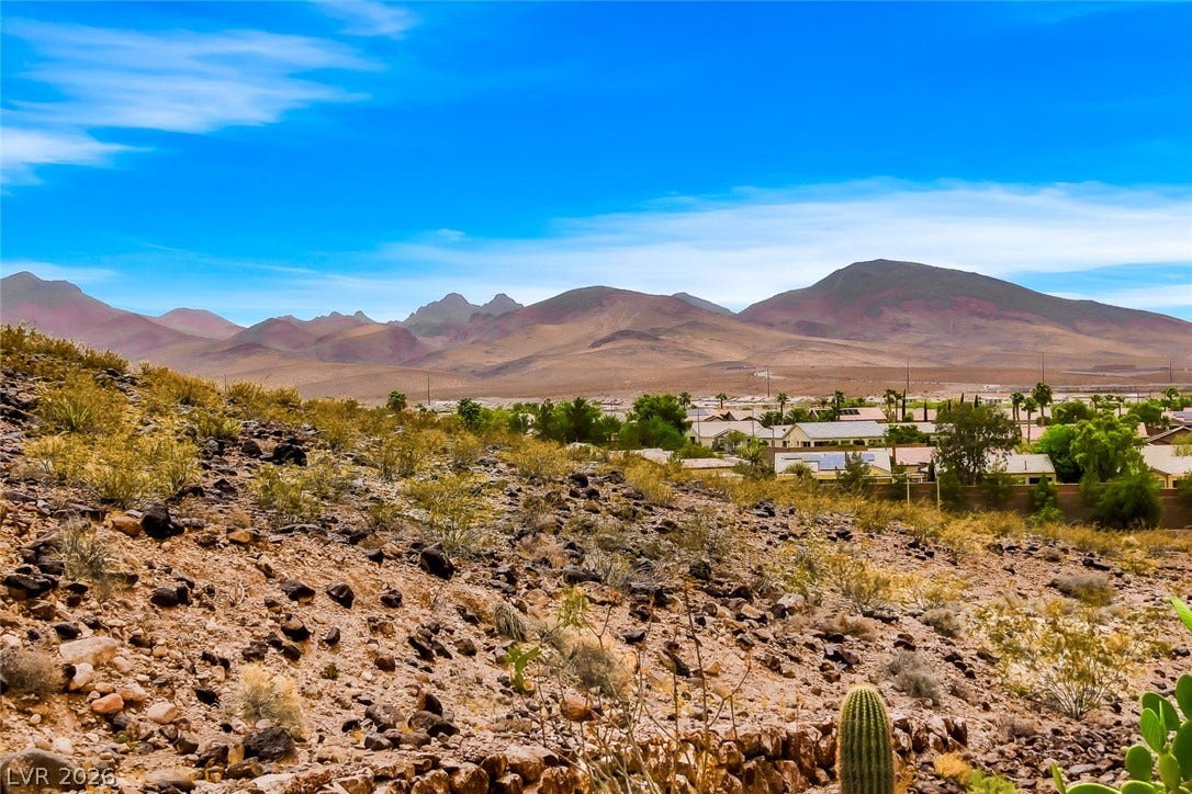2306 Schaeffer Hills Drive, Henderson, NV 89052 A desert landscape unfolds with distant mountains, a community nestled in the valley, and a clear blue sky overhead.
