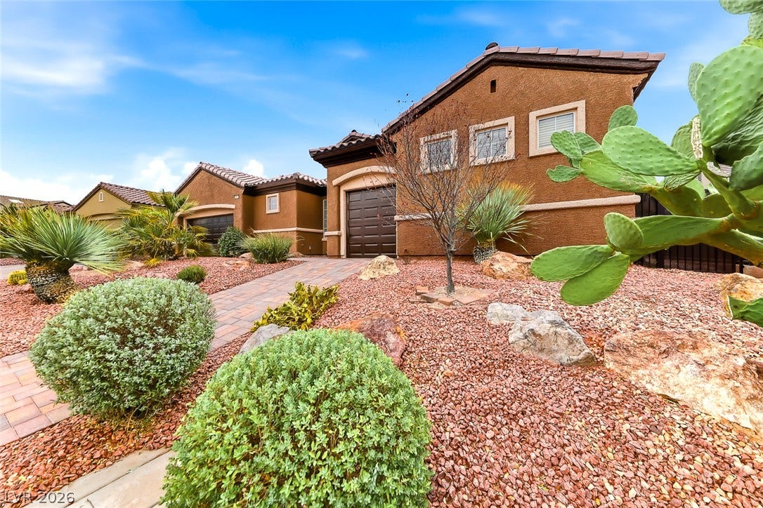 2306 Schaeffer Hills Drive, Henderson, NV 89052 A terracotta-hued residence welcomes with a paved walkway, leading through a desert-inspired landscape of gravel, shrubs, and succulents.