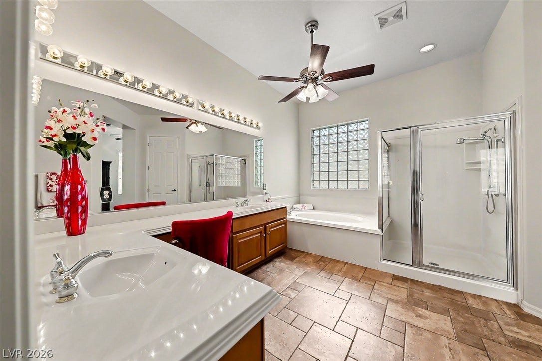 2306 Schaeffer Hills Drive, Henderson, NV 89052 A well-appointed primary bathroom featuring a large vanity, glass-block window, and an inviting soaking tub with an adjacent shower.