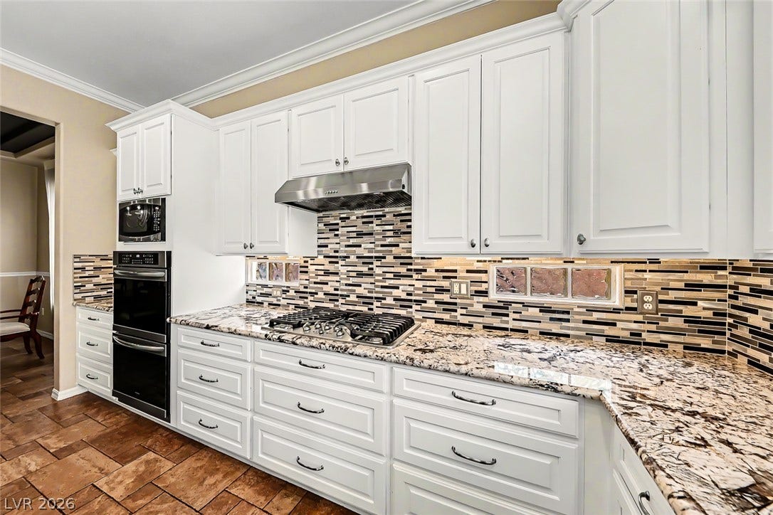 2306 Schaeffer Hills Drive, Henderson, NV 89052 White cabinetry complements granite countertops and a tiled backsplash in this well-appointed kitchen.