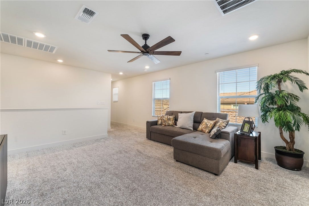 2966 Gallarate Drive, Henderson, NV 89044 A well-lit sitting area with soft carpet features a modern ceiling fan and natural light from large windows.