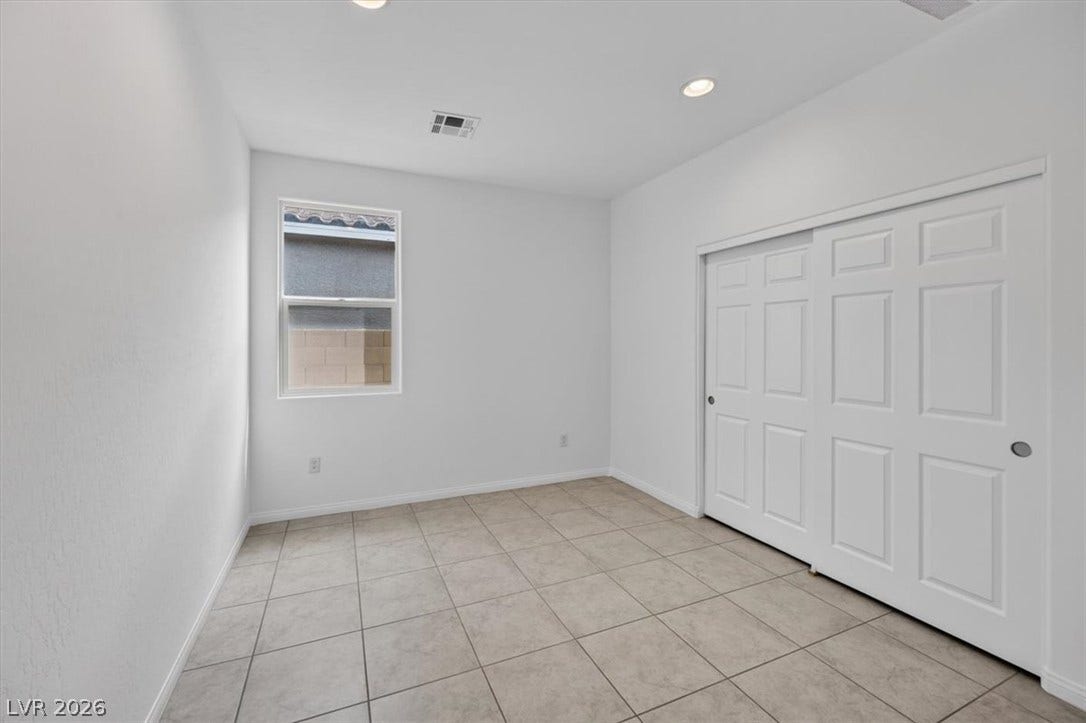 A well-lit bedroom features durable tile flooring and convenient sliding closet doors.