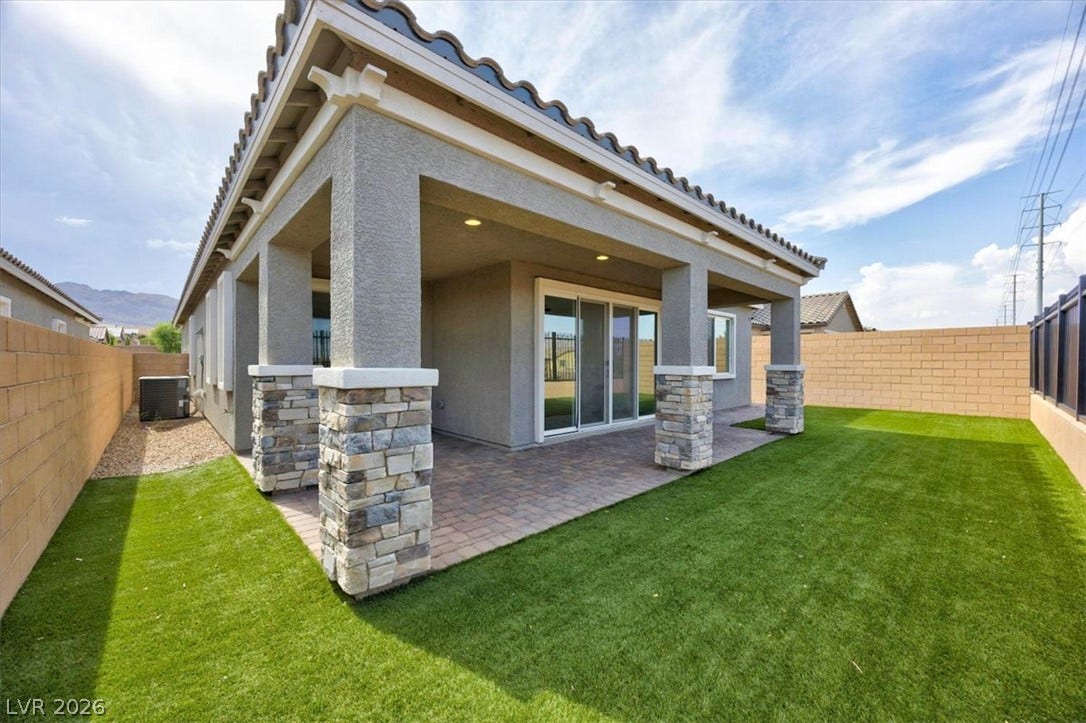 A spacious covered patio with sturdy stone-clad pillars overlooks a vibrant green lawn, ideal for outdoor leisure.