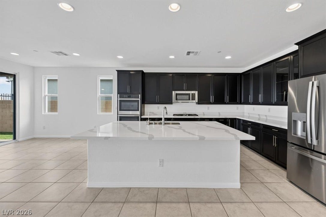 A well-appointed kitchen features stainless steel appliances, dark cabinetry, and a spacious central island with a sink.