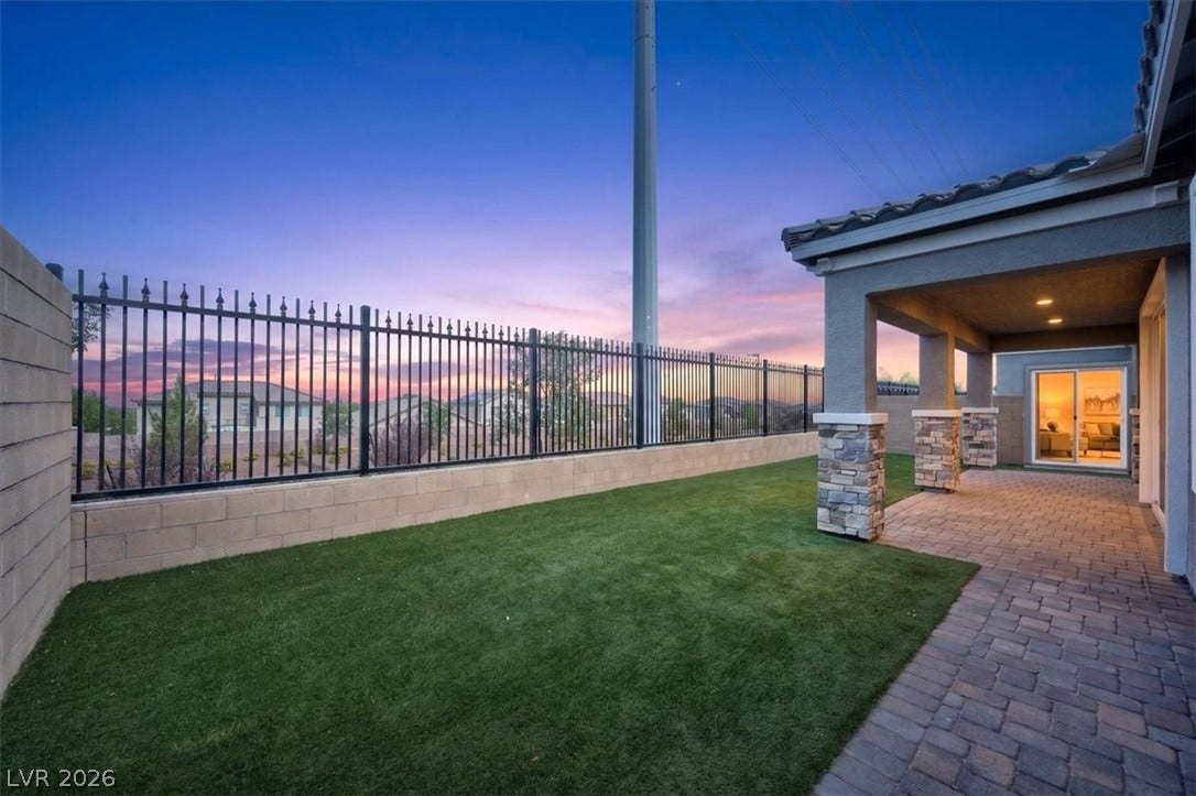An inviting covered patio and lush green lawn offer serene outdoor living at twilight.