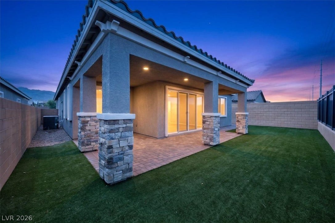A spacious covered patio with stone-accented pillars overlooks a verdant lawn, ideal for outdoor gatherings.