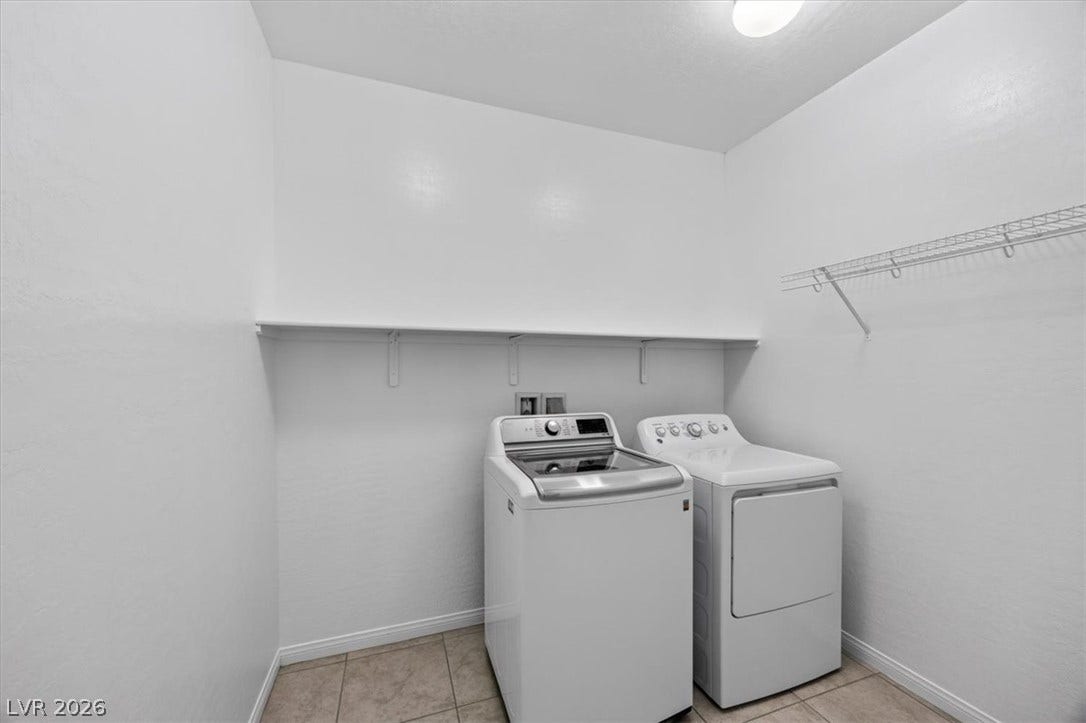 Functional laundry room featuring tile flooring, convenient shelving, and included appliances for effortless chores.