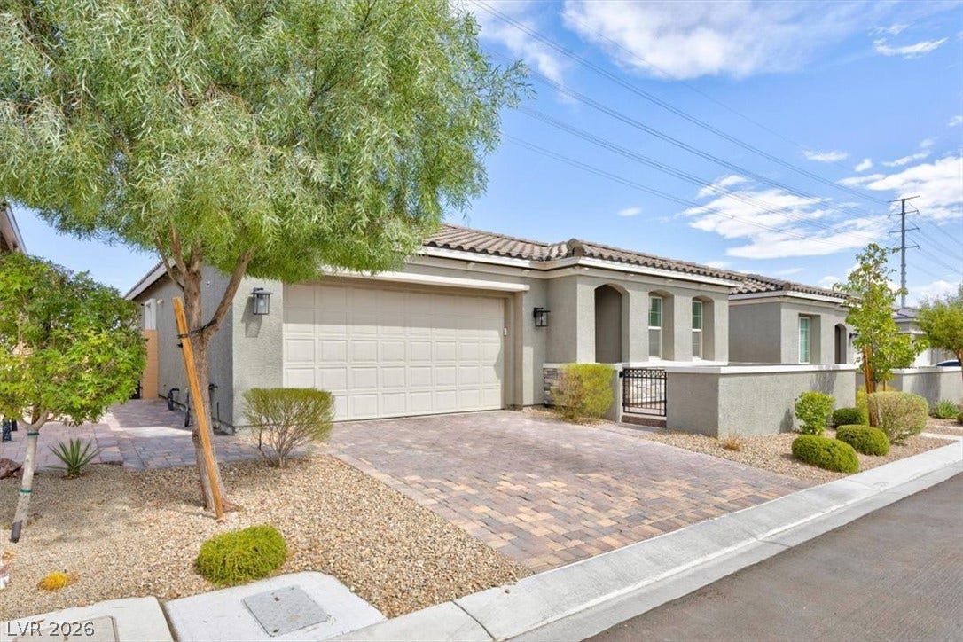 A well-maintained stucco home with a tiled roof, paver driveway, and desert-friendly landscaping.