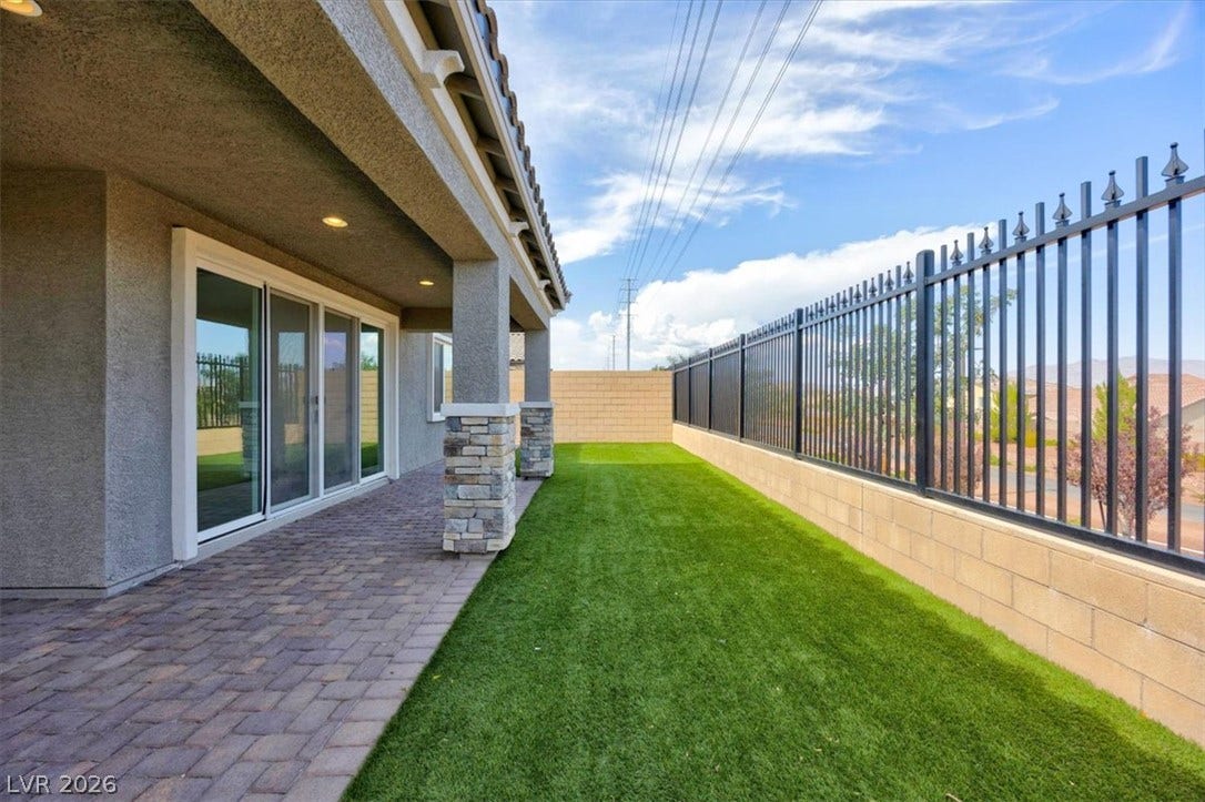 A spacious covered patio with pavers extends to a vibrant green turf yard, enclosed by secure fencing.