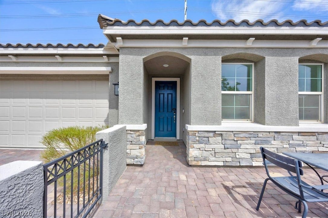 A welcoming stone and stucco facade greets guests with a bright blue entry door and paver patio.