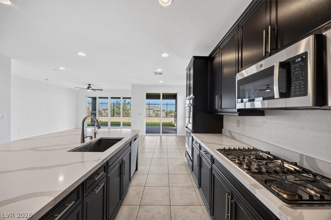 Modern kitchen with sleek dark cabinetry, white countertops, and contemporary appliances, flowing into an open living area with outdoor access.