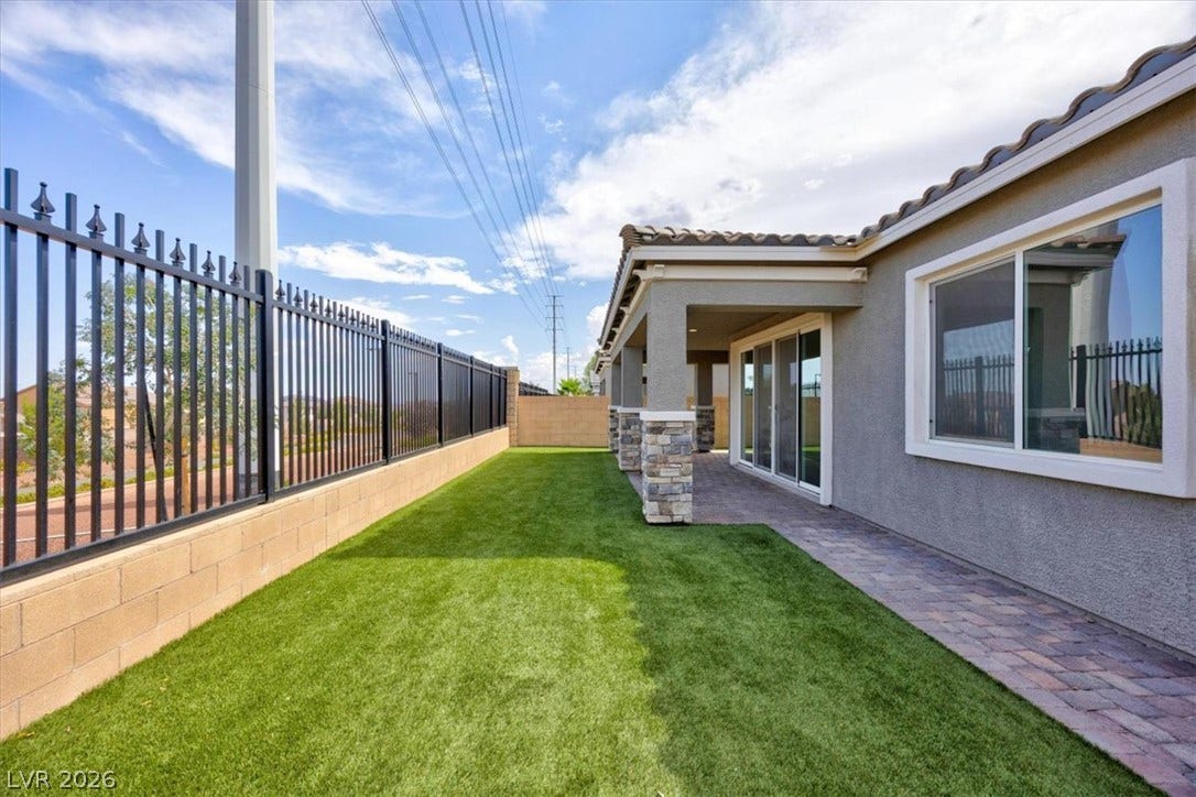 An inviting backyard oasis awaits with artificial turf, a tiled patio, and elegant stone columns.