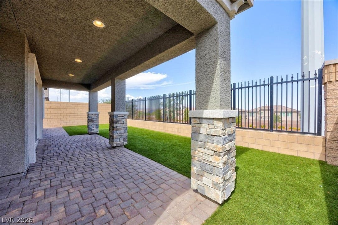A spacious covered patio with stone-accented pillars and paver flooring offers a perfect outdoor retreat.