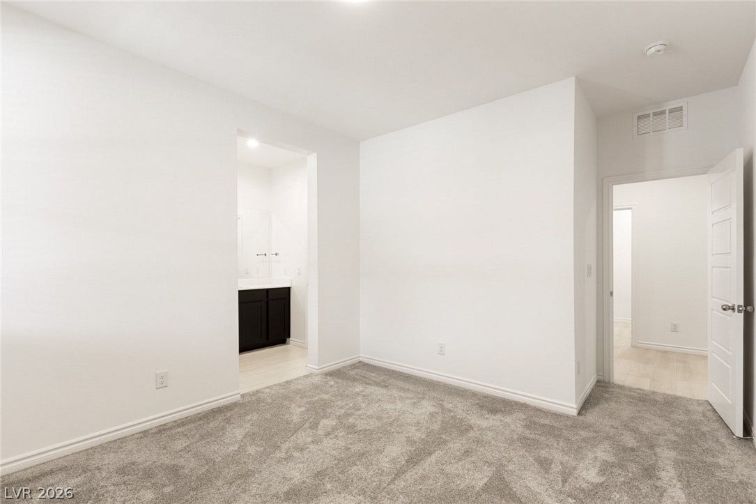 9986 Joshua Foothills Street, Las Vegas, NV 89178 Well-lit room with neutral finishes and plush carpeting, offering a seamless transition to a private bathroom with a dark vanity.