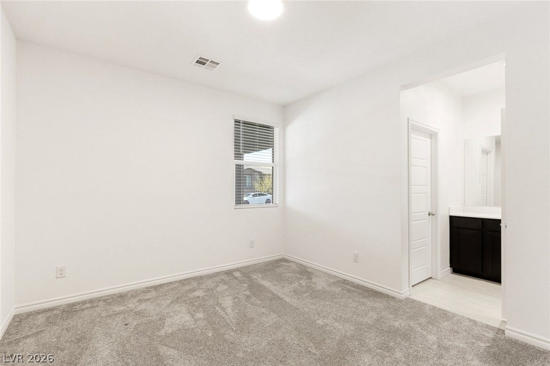 9986 Joshua Foothills Street, Las Vegas, NV 89178 A well-lit bedroom with plush carpeting leads into a private bathroom.