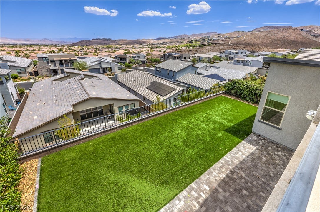 1984 Canyon Highlands Drive, Henderson, NV 89052 A tiered backyard with lush artificial turf and paver patio overlooks a scenic desert landscape and residential community.