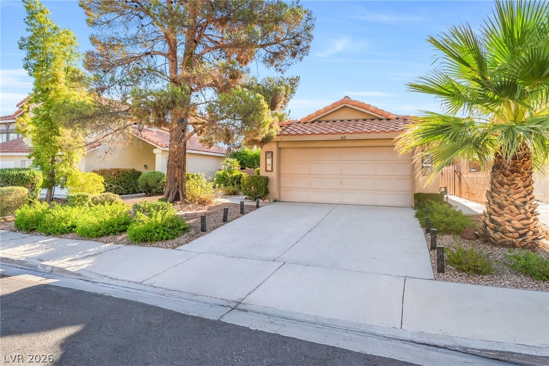 62 Tidwell Lane, Henderson, NV 89074 Mature trees and neat low-water landscaping frame a wide concrete driveway leading to the garage.
