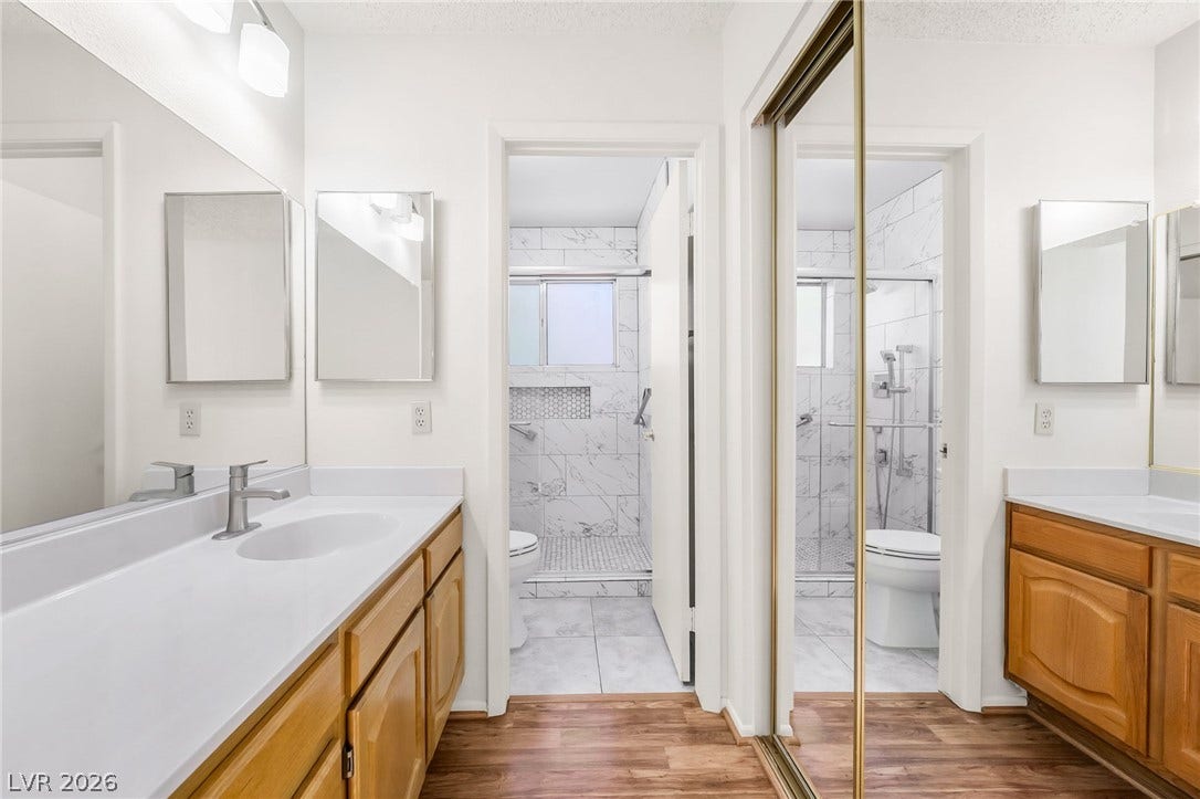 62 Tidwell Lane, Henderson, NV 89074 Double vanities with wood cabinetry flank a central walkway leading to a tiled shower.