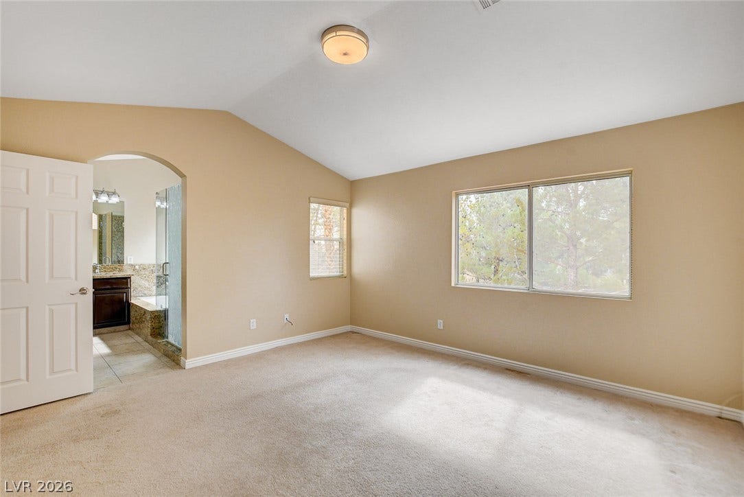 1612 Country Hollow Drive, Las Vegas, NV 89117 A spacious primary bedroom features soft carpeting, vaulted ceilings, and an arched entry to an en-suite bathroom.