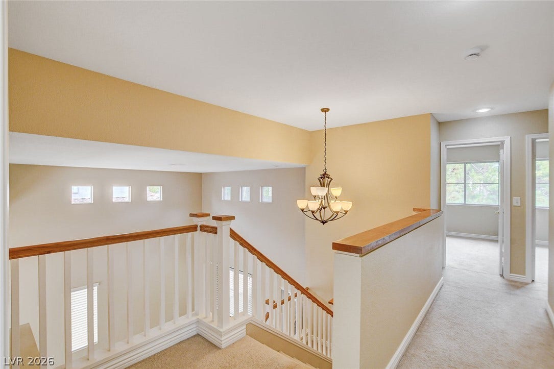 1612 Country Hollow Drive, Las Vegas, NV 89117 A graceful staircase with warm wood accents leads to a bright upper landing, illuminated by a classic chandelier.