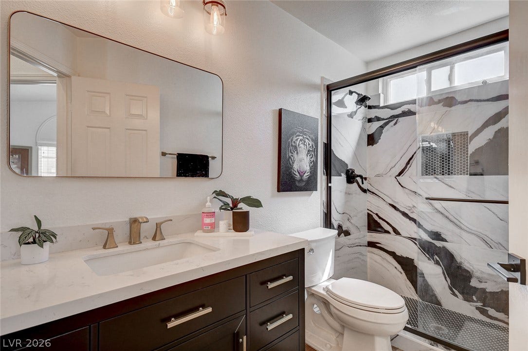 236 Misty Garden Street, Henderson, NV 89012 A stylish bathroom features a dark vanity topped with stone counters and a patterned walk-in shower.