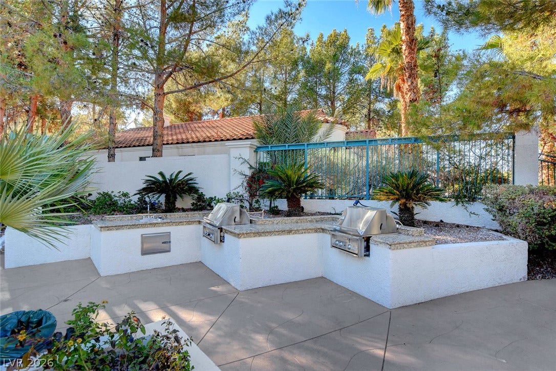 236 Misty Garden Street, Henderson, NV 89012 Custom outdoor kitchen features built-in grills, stone countertops, and a concrete patio among lush trees.
