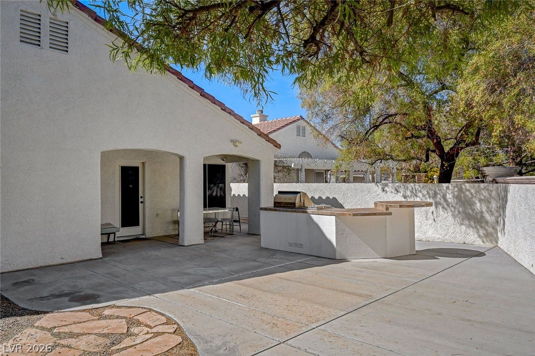 236 Misty Garden Street, Henderson, NV 89012 An expansive concrete patio features a built-in outdoor kitchen under mature shade trees.
