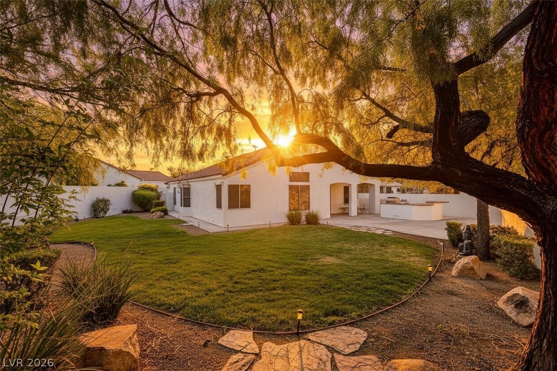 236 Misty Garden Street, Henderson, NV 89012 Mature trees frame a manicured lawn and stone pathway under a glowing evening sky.