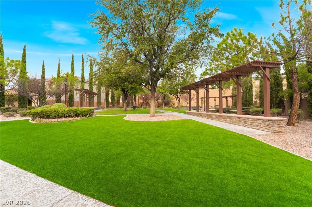 11416 Rancho Portena Avenue, Las Vegas, NV 89138 Manicured green space features stone retaining walls and wooden shade structures under a clear sky.